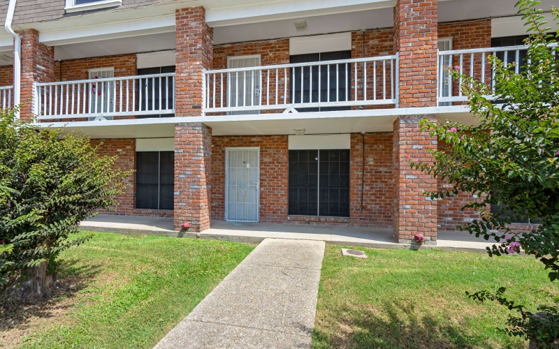 Front view of a charming apartment building with a brick facade, featuring private balconies and manicured shrubbery in the foreground.